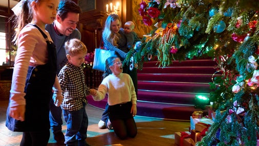 Alice's Christmas in Wonderland at Polesden Lacey 2025: a young family admire a large, lavishly decorated Christmas tree on the main hall